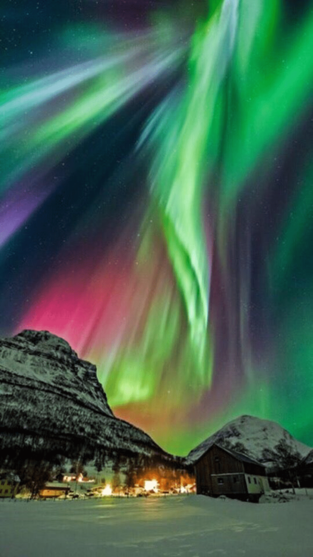 multicoloured bands of light across the night sky in mountainous night scene with buildings