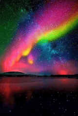 multicoloured bands of light across a star-filled sky beneath open sky above a low, dark horizon and reflective surface