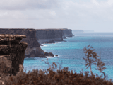 coastline of tall rocky sea cliffs beside turquoise-blue ocean water Ocean waves break gently